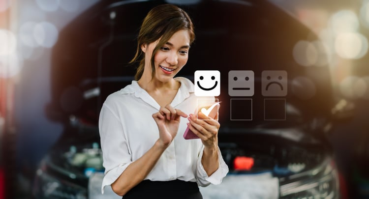 Auto repair shop customer, smiling at her phone, selecting a smiley face in reaction to excellent customer service.