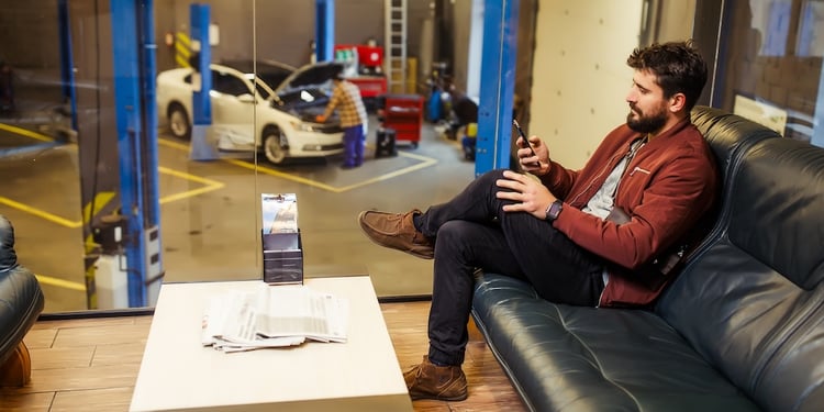 Man sitting on a leather couch playing on his phone in an auto repair shop waiting room.