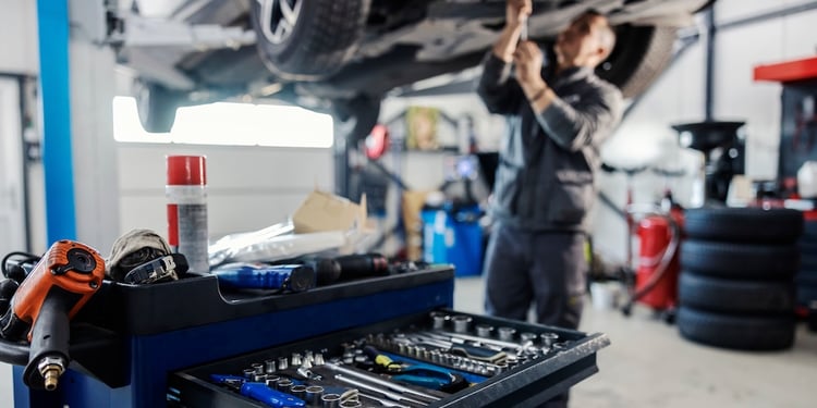 An automotive technician's tool box in focus displaying a variety of wrenches while an automotive technicians works under a vehicle in the background
